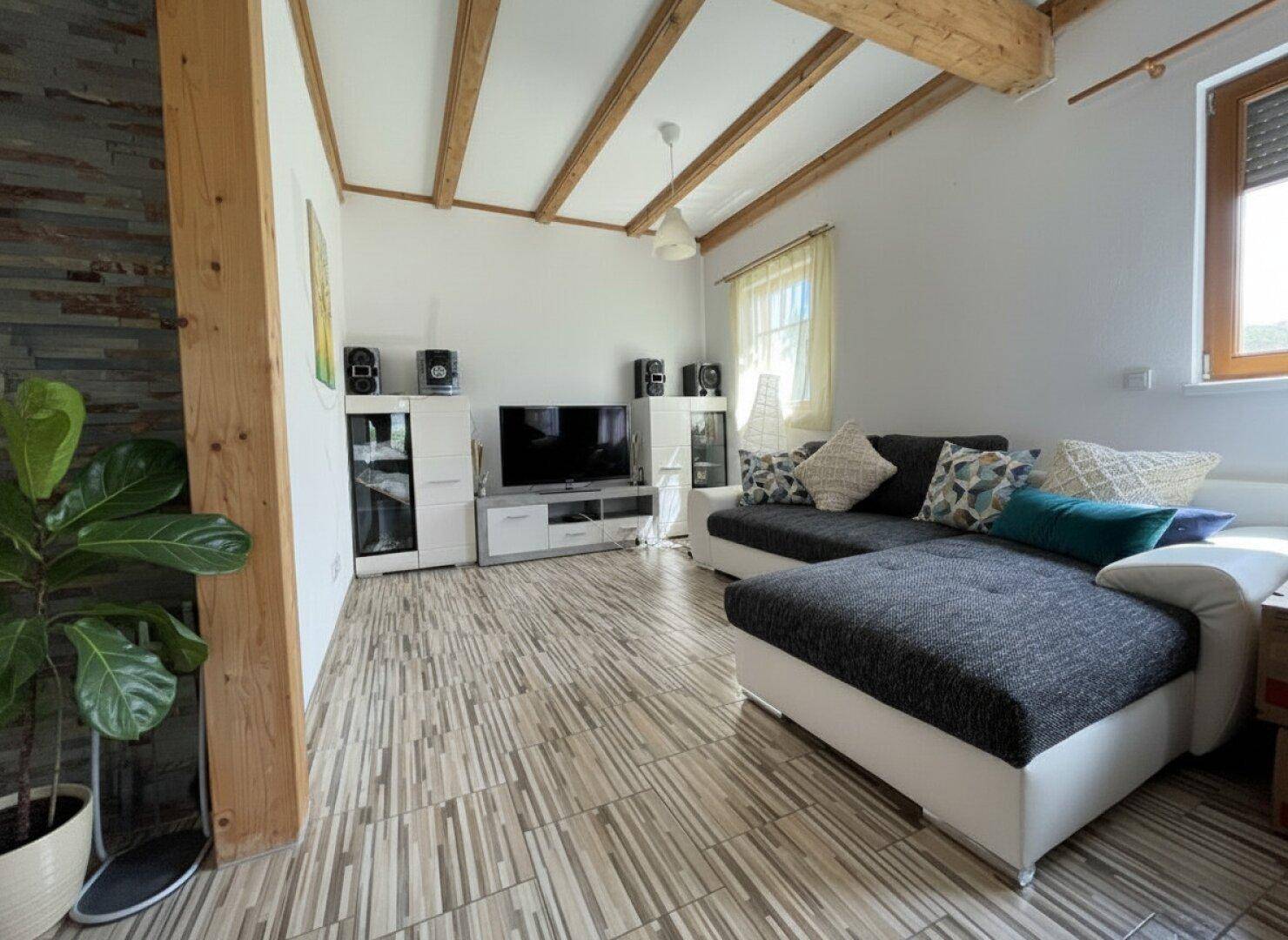Gemütliches Wohnzimmer mit großem Ecksofa, Fliesenboden und Holzbalkendecke.