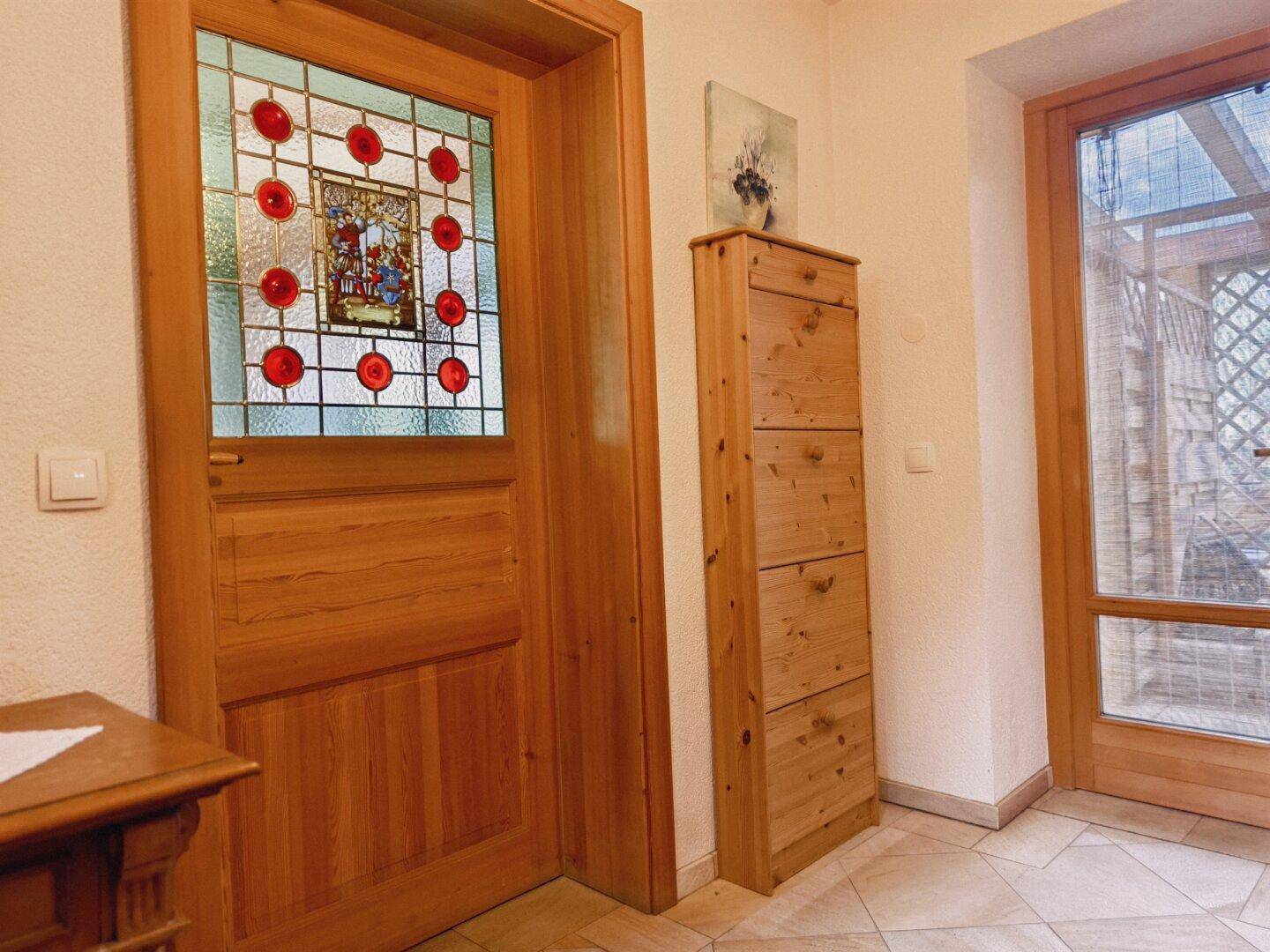 Heller Eingangsbereich mit Holztür, Buntglasfenster und praktischem Schuhschrank.