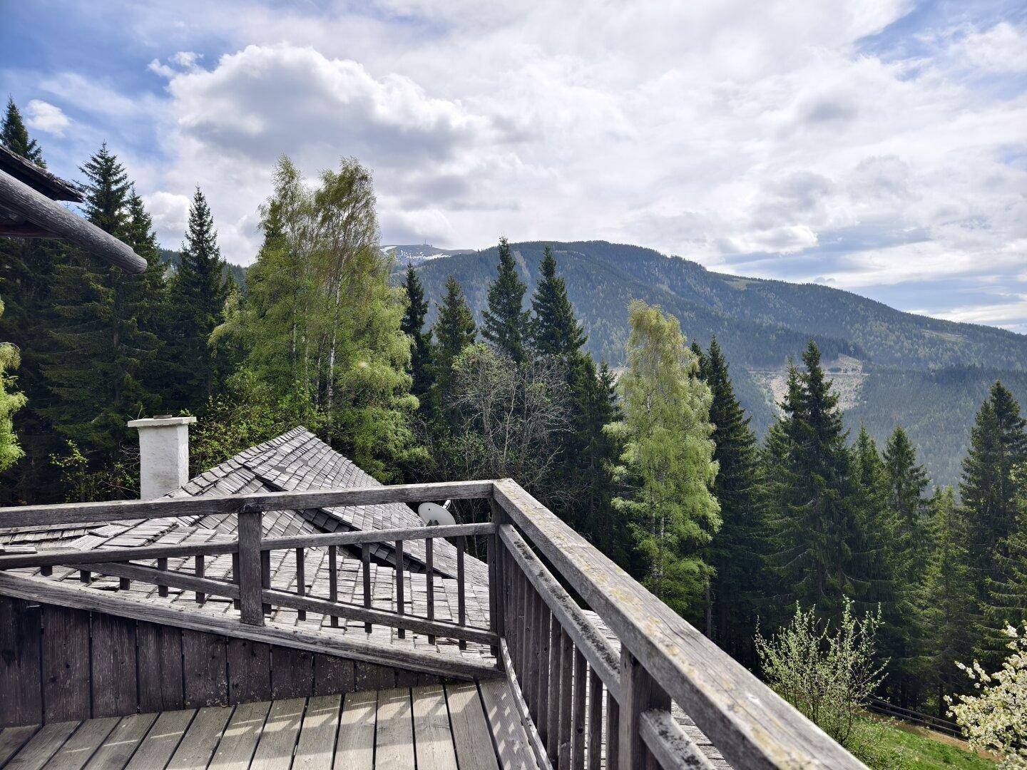 Panoramablick vom Holzbalkon auf die weite Berglandschaft und grüne Wälder.