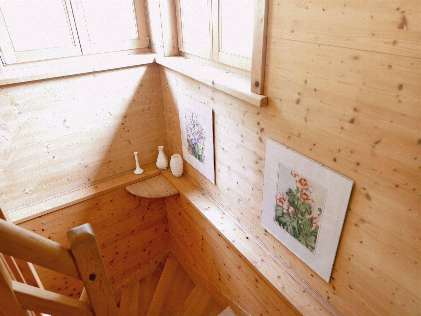 Helle Holztreppe mit natürlichem Lichteinfall und floralen Bildern an den Wänden.