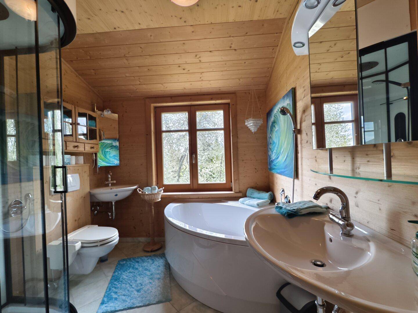 Geräumiges Badezimmer mit Duschkabine, Badewanne und zwei Waschbecken in Holzoptik.