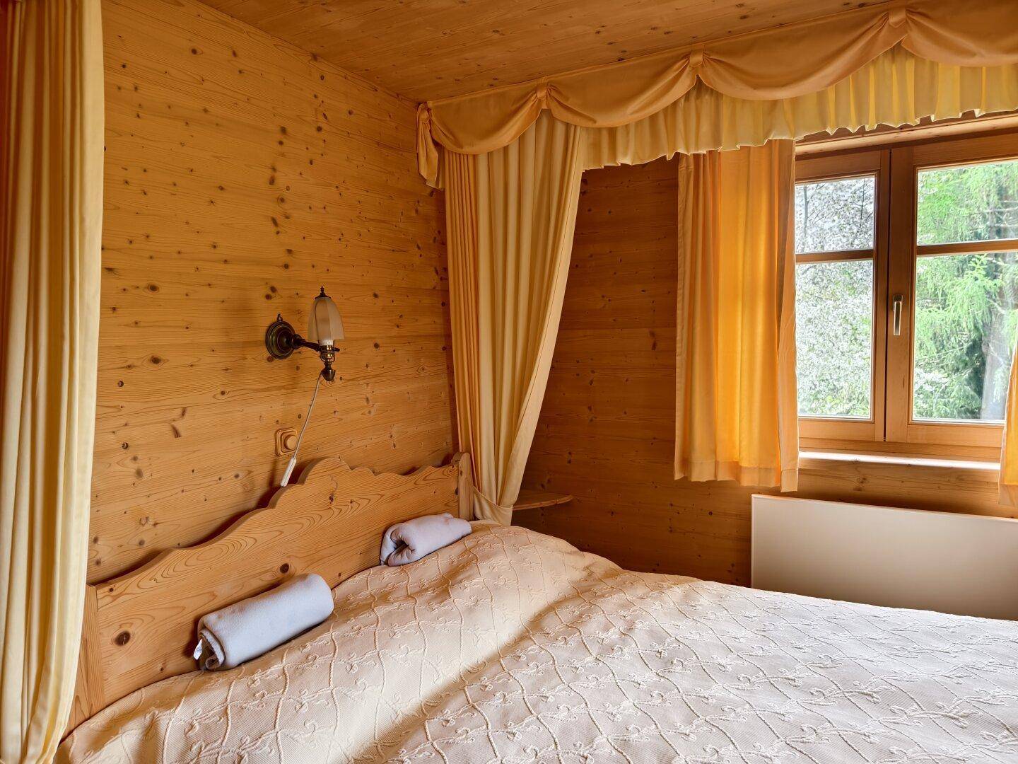 Gemütliches Schlafzimmer mit Holzvertäfelung, Doppelbett und traditionellen Vorhängen.