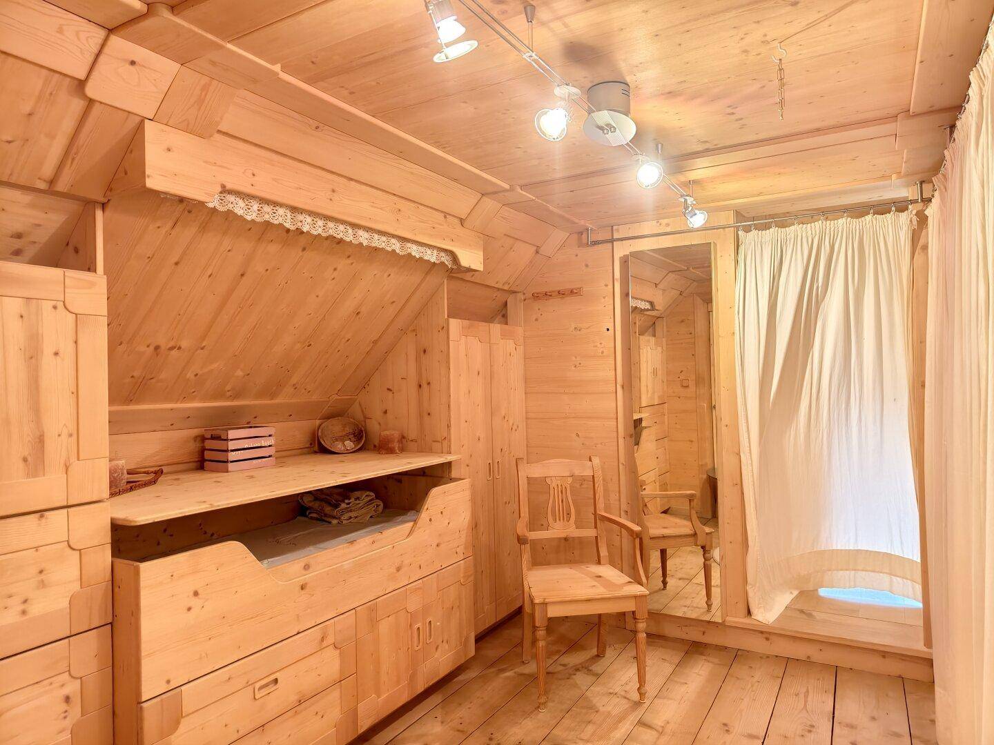 Gemütliches Schlafzimmer im Dachgeschoss mit Holzvertäfelung und integrierten Möbeln.