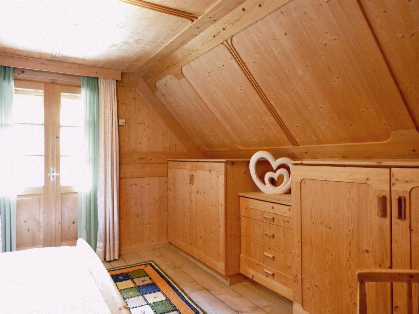 Gemütliches Schlafzimmer im Dachgeschoss mit Holzvertäfelung, Einbauschränken und Zugang zum Balkon.