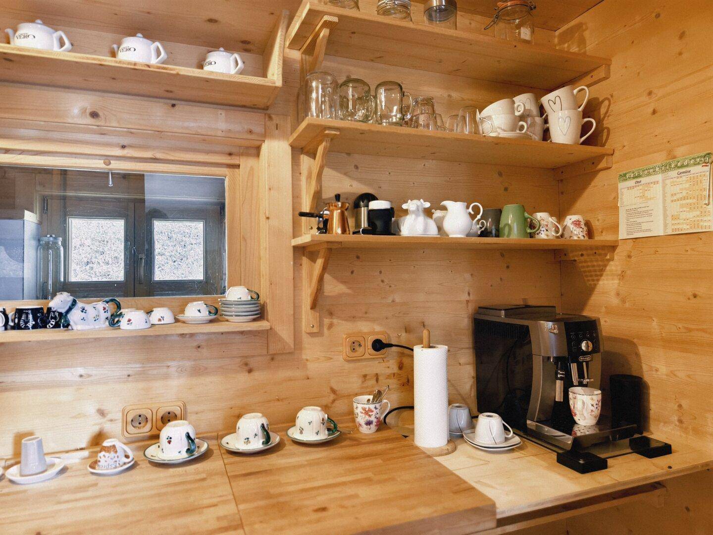Detailansicht der Holzküche mit Kaffeemaschine, Geschirr und offenen Regalen.