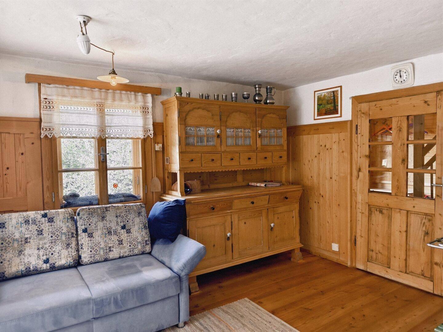 Gemütliches Wohnzimmer im Landhausstil mit Sofa, Holzmöbeln und Fensterblick.