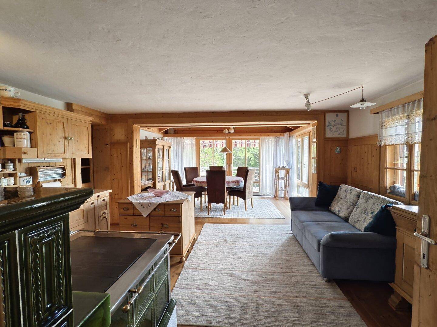 Großzügiger Wohn- und Essbereich mit Kachelofen, Sofa und Zugang zur Terrasse.