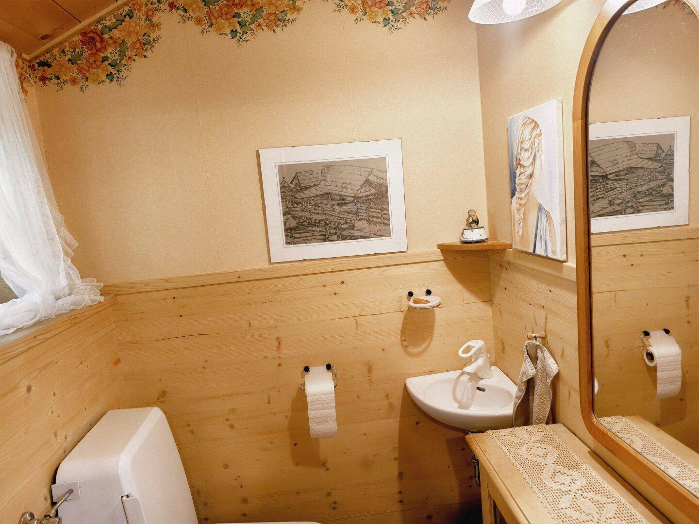 Kleines Gäste-WC mit Holzvertäfelung, Waschbecken und floraler Tapetenbordüre.