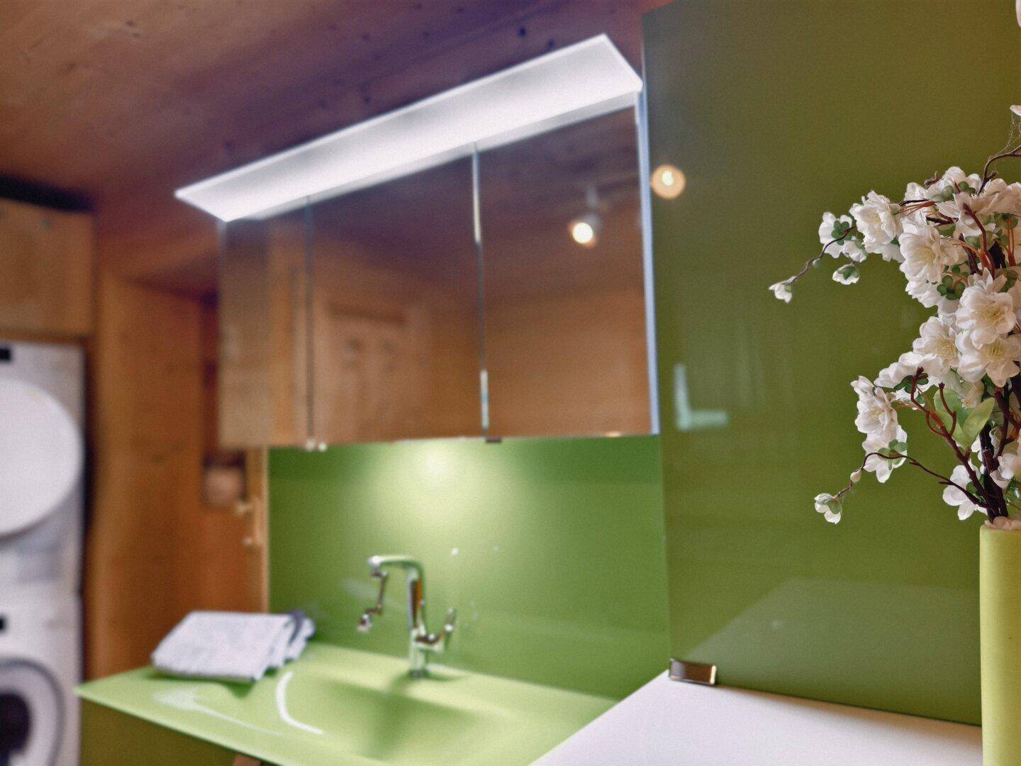Modernes Badezimmer mit grünem Waschtisch, Spiegelschrank und Waschmaschine.