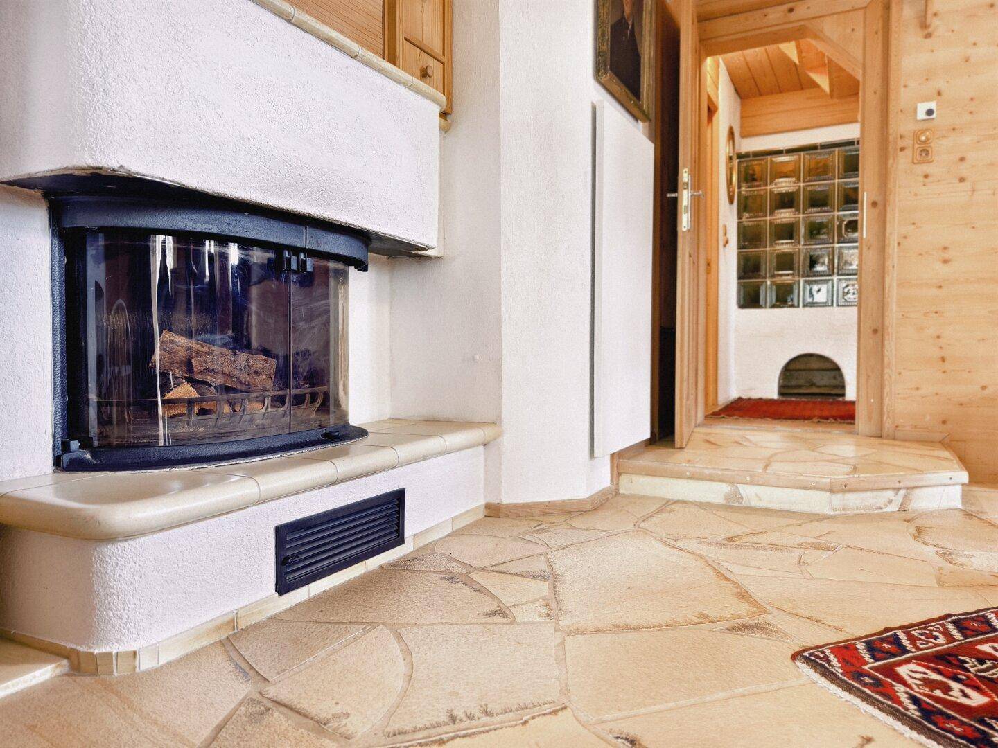 Eingangsbereich mit Kamin, Fliesenboden und Blick auf einen weiteren Raum.