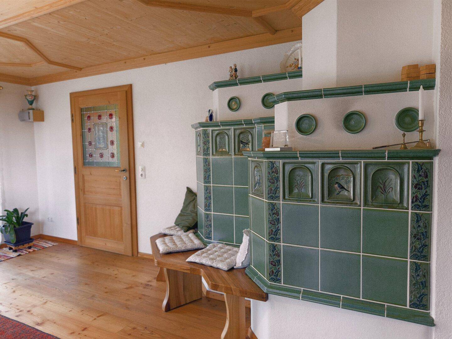 Geräumiger Wohnbereich mit grünem Kachelofen, Holzboden und dekorativer Decke.