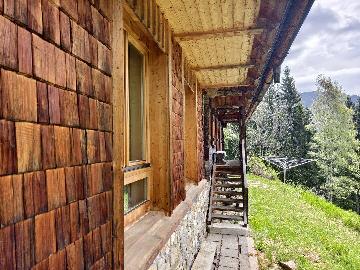 Rustikale Holzfassade eines Chalets mit Balkon und Blick auf die grüne Landschaft.