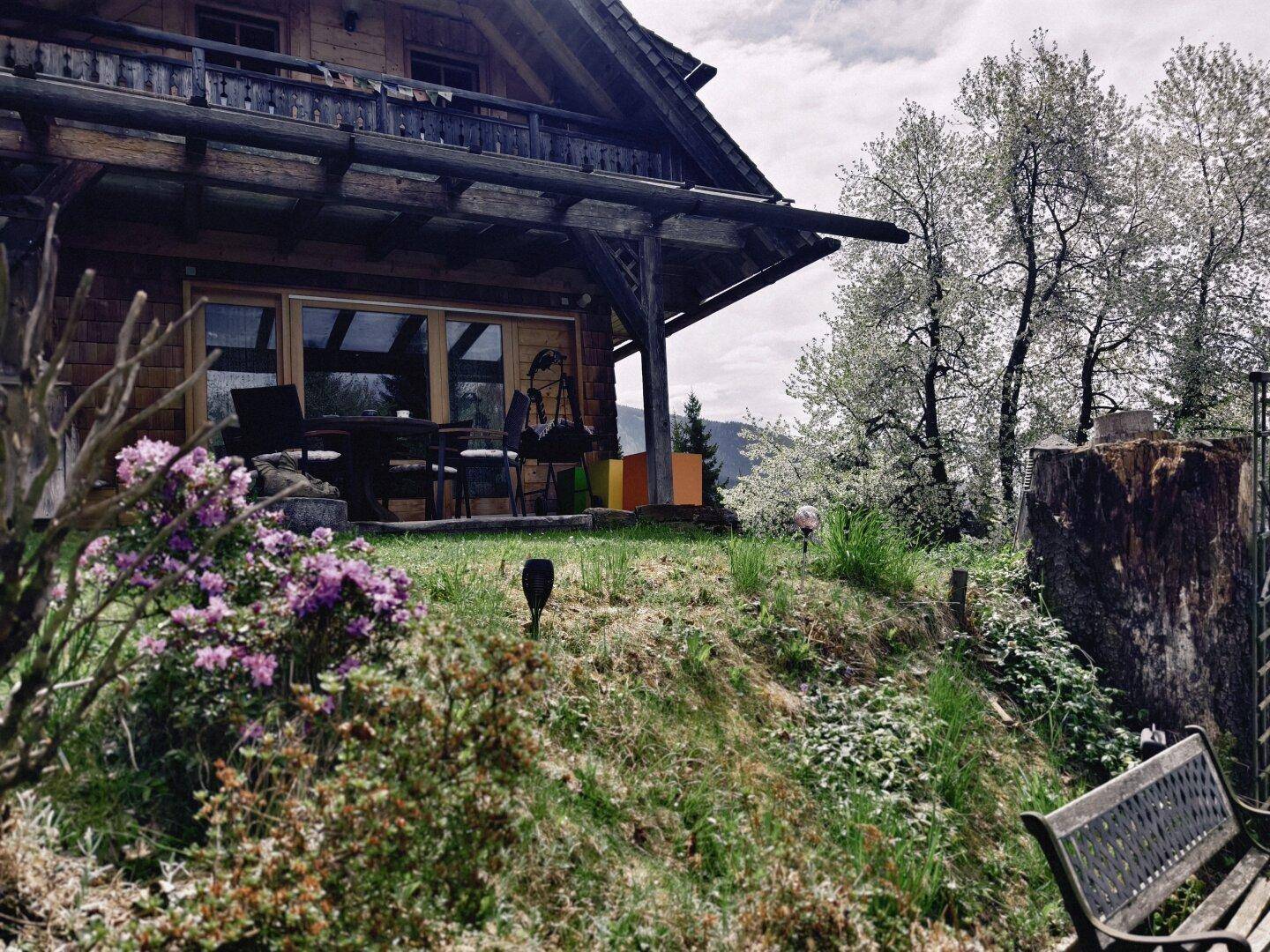 Gartenbereich mit Sitzgelegenheiten, blühenden Pflanzen und Blick auf das Chalet.