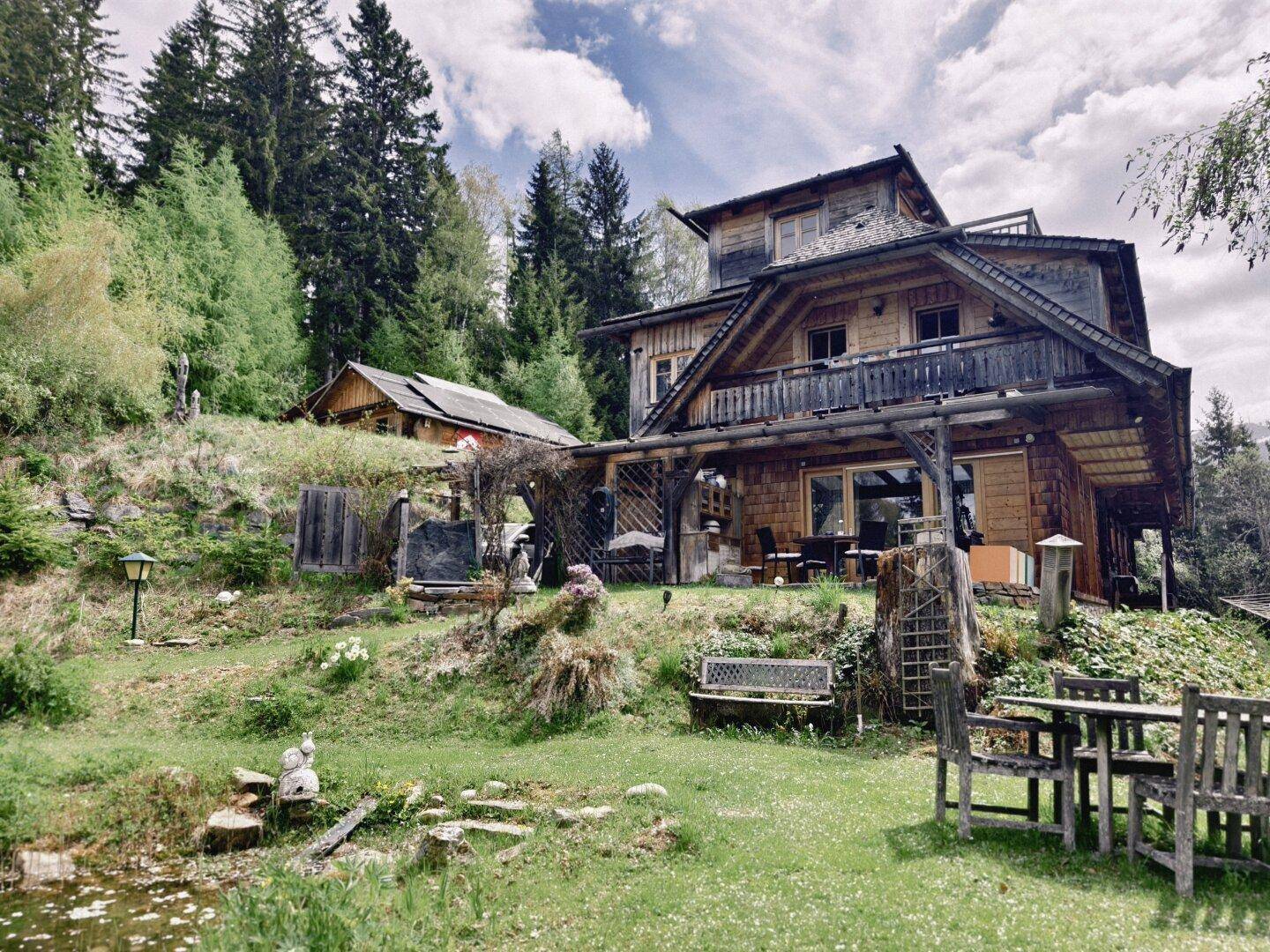 Rustikales Holzhaus mit großem Gartenbereich, Sitzgelegenheiten und Blick auf die umliegenden Wälder.