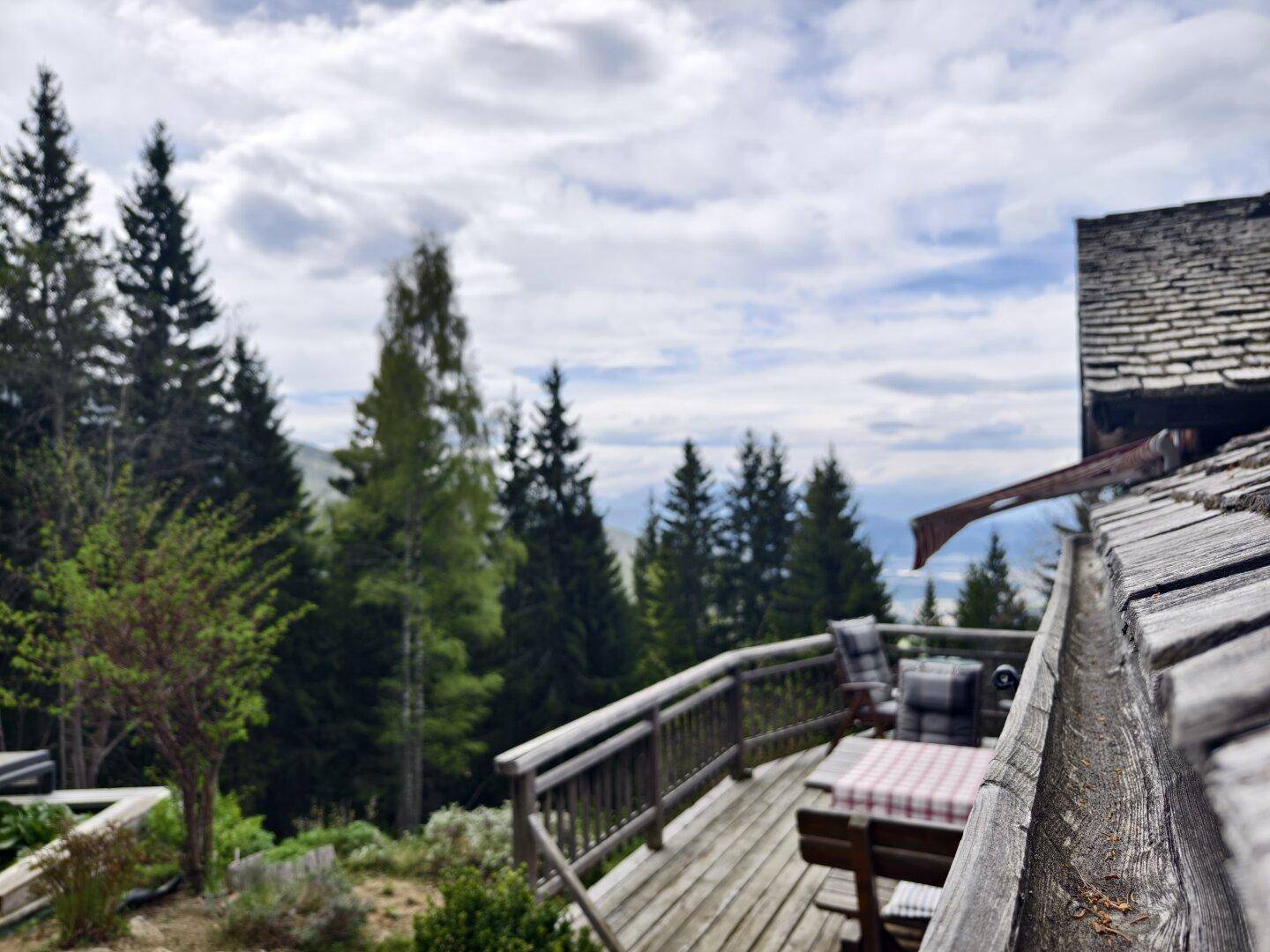Holzterrasse mit rustikalem Geländer und Sitzbereich, bietet einen weiten Blick auf die bewaldete Berglandschaft.