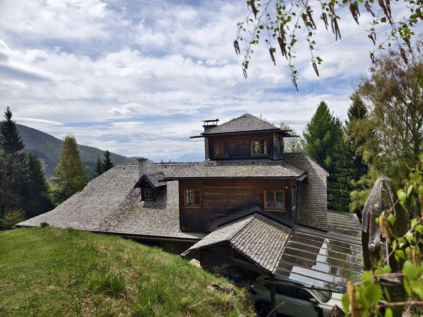 Charmantes Holzhaus mit traditioneller Architektur und Schindeldach, umgeben von grüner Natur und Bergen.