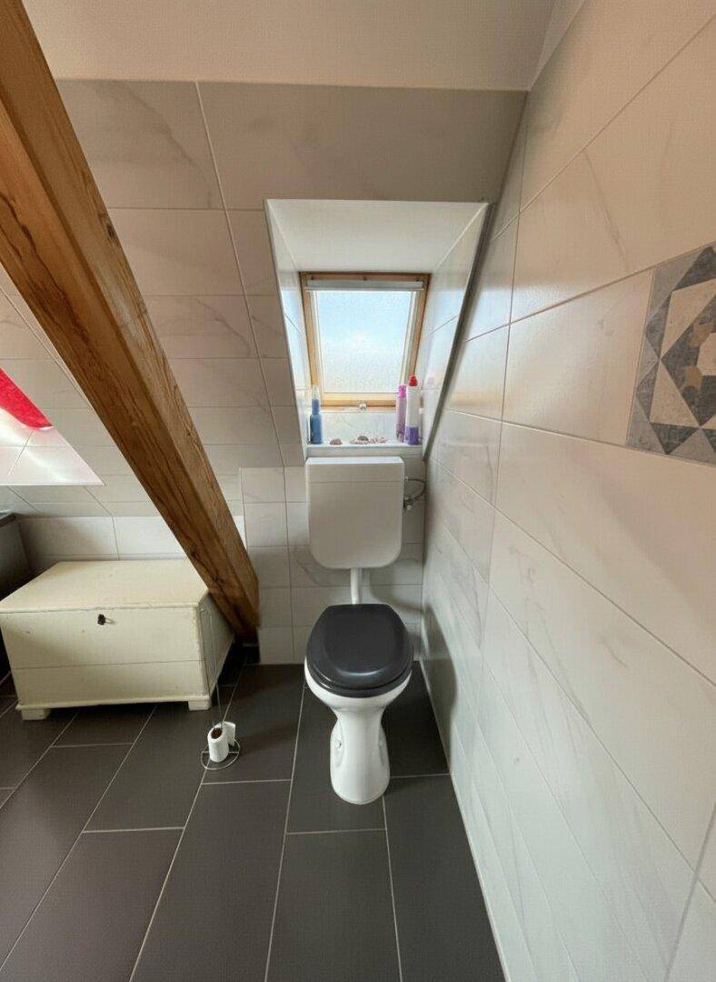 Toilette im Dachgeschoss-Badezimmer mit Dachfenster und schrägen Wänden.