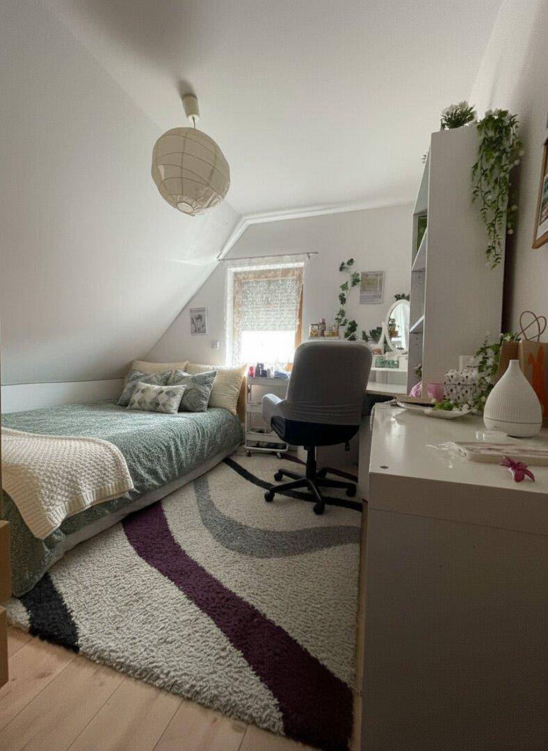 Gemütliches Schlafzimmer im Dachgeschoss mit Bett, Schreibtisch und Teppichboden.