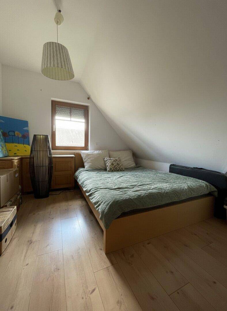 Schlafzimmer im Dachgeschoss mit Holzboden, Bett und schrägen Wänden.