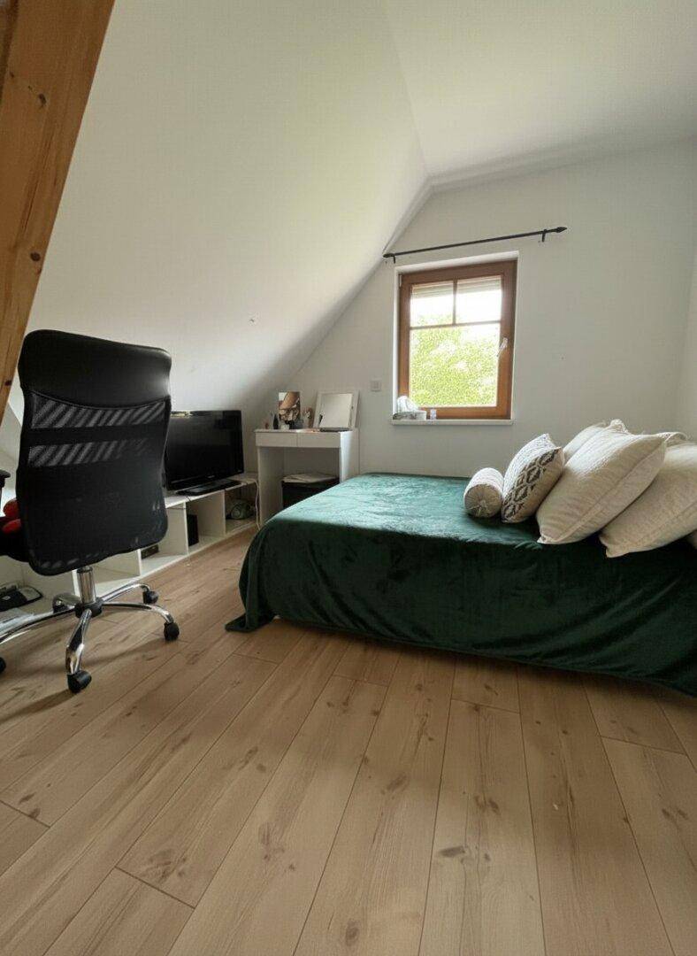 Helles Schlafzimmer im Dachgeschoss mit Bett, Schreibtisch und Laminatboden.