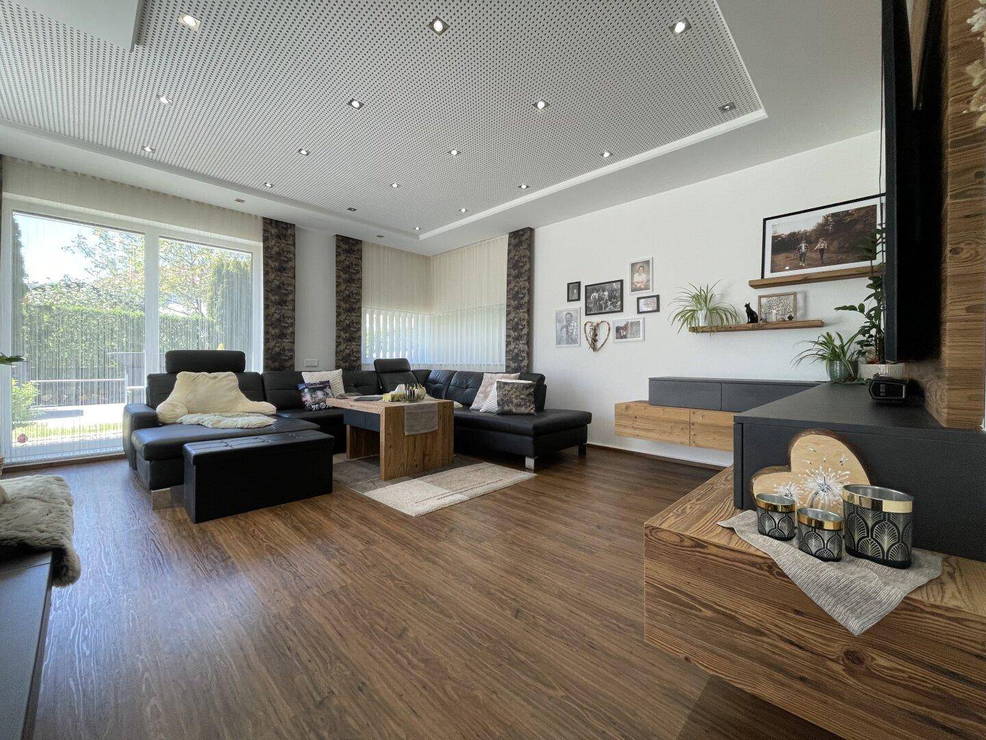 Modernes Wohnzimmer mit dunklem Sofa, Holzboden und perforierter Decke mit integrierten Lichtern.