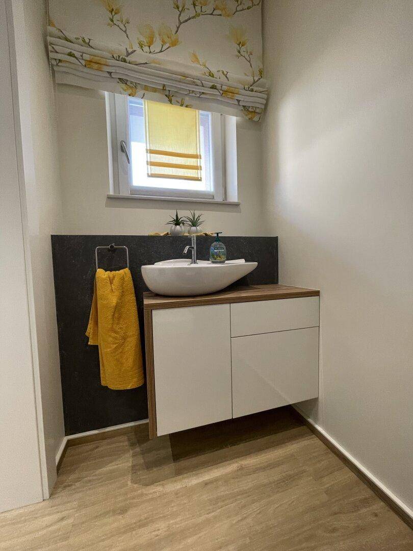 Modernes Gäste-WC mit stilvollem Waschbecken, Holzunterschrank und Fenster.