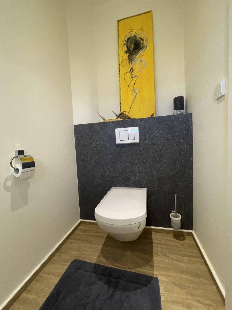 Modernes Gäste-WC mit wandmontierter Toilette und künstlerischer Wanddekoration.