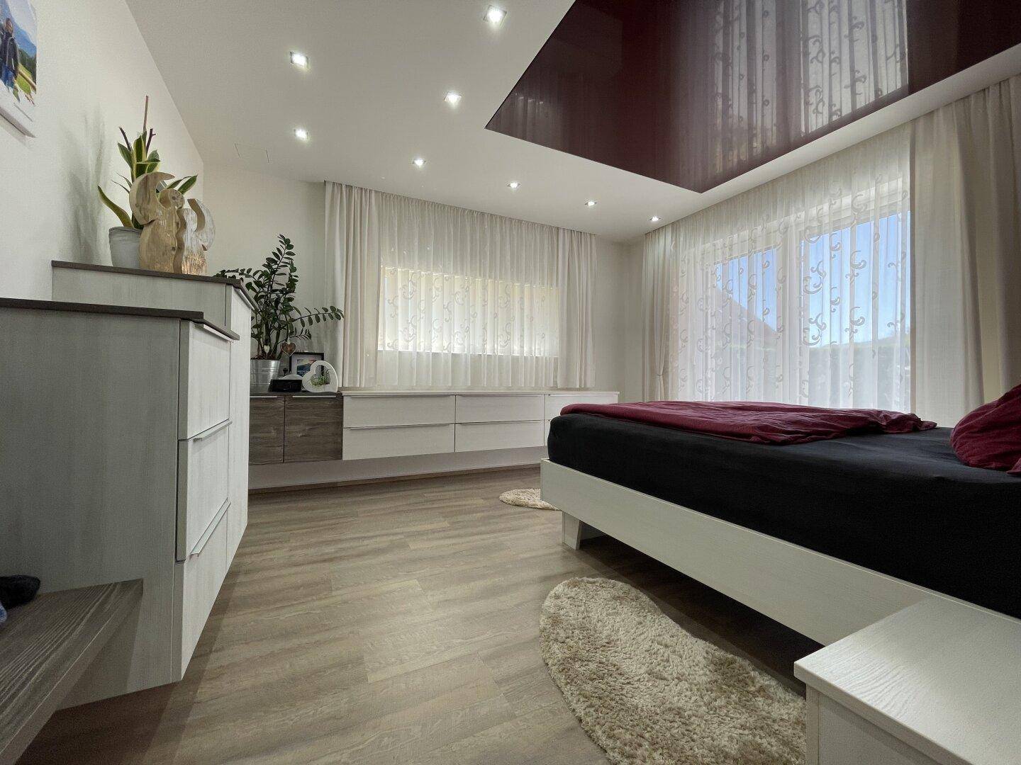 Helles Schlafzimmer mit modernem Bett, Einbauschränken und großen Fenstern, die viel Tageslicht hereinlassen.