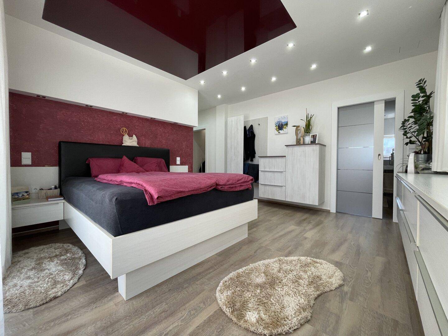 Modernes Schlafzimmer mit großem Bett, Einbauschränken und einer roten Akzentwand, die dem Raum Charakter verleiht.