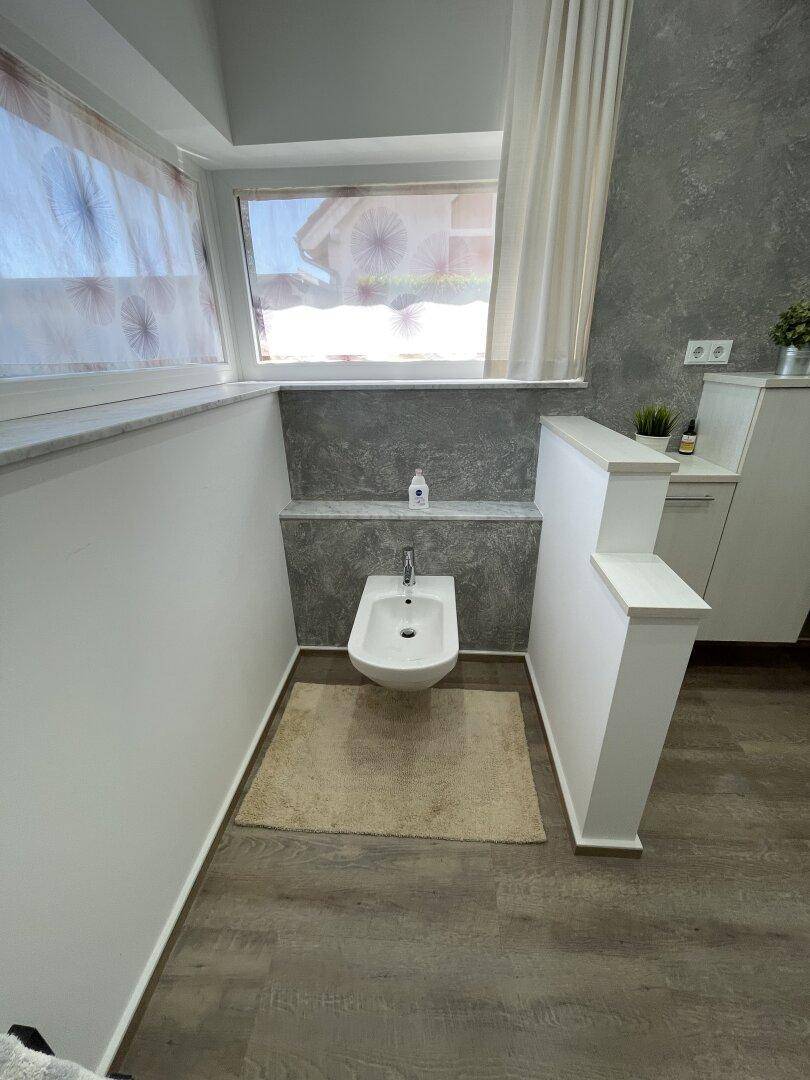 Modernes Bidet in einem Badezimmer, strategisch unter einem Fenster platziert, für optimale Belüftung und Licht.