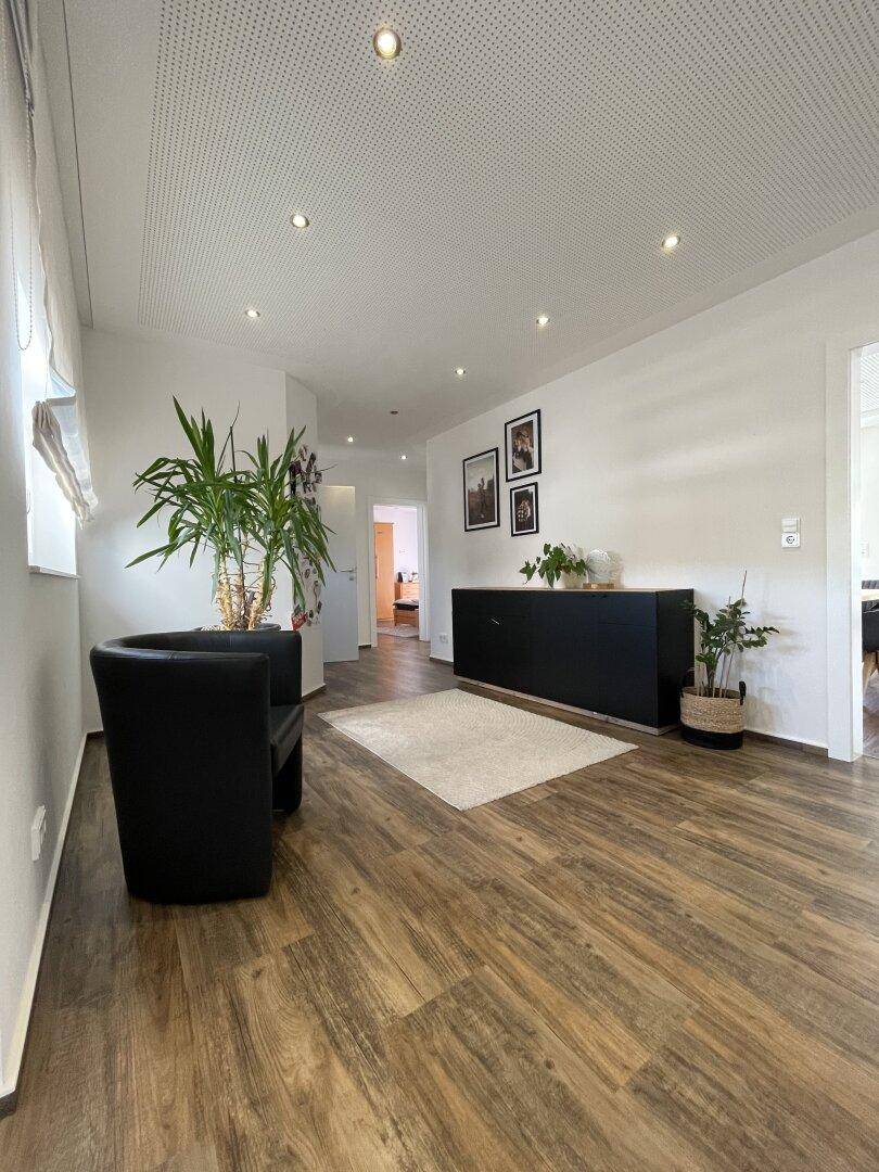 Heller Flur mit Holzoptikboden, einem schwarzen Sideboard und einer großen Zimmerpflanze, die Frische verleiht.