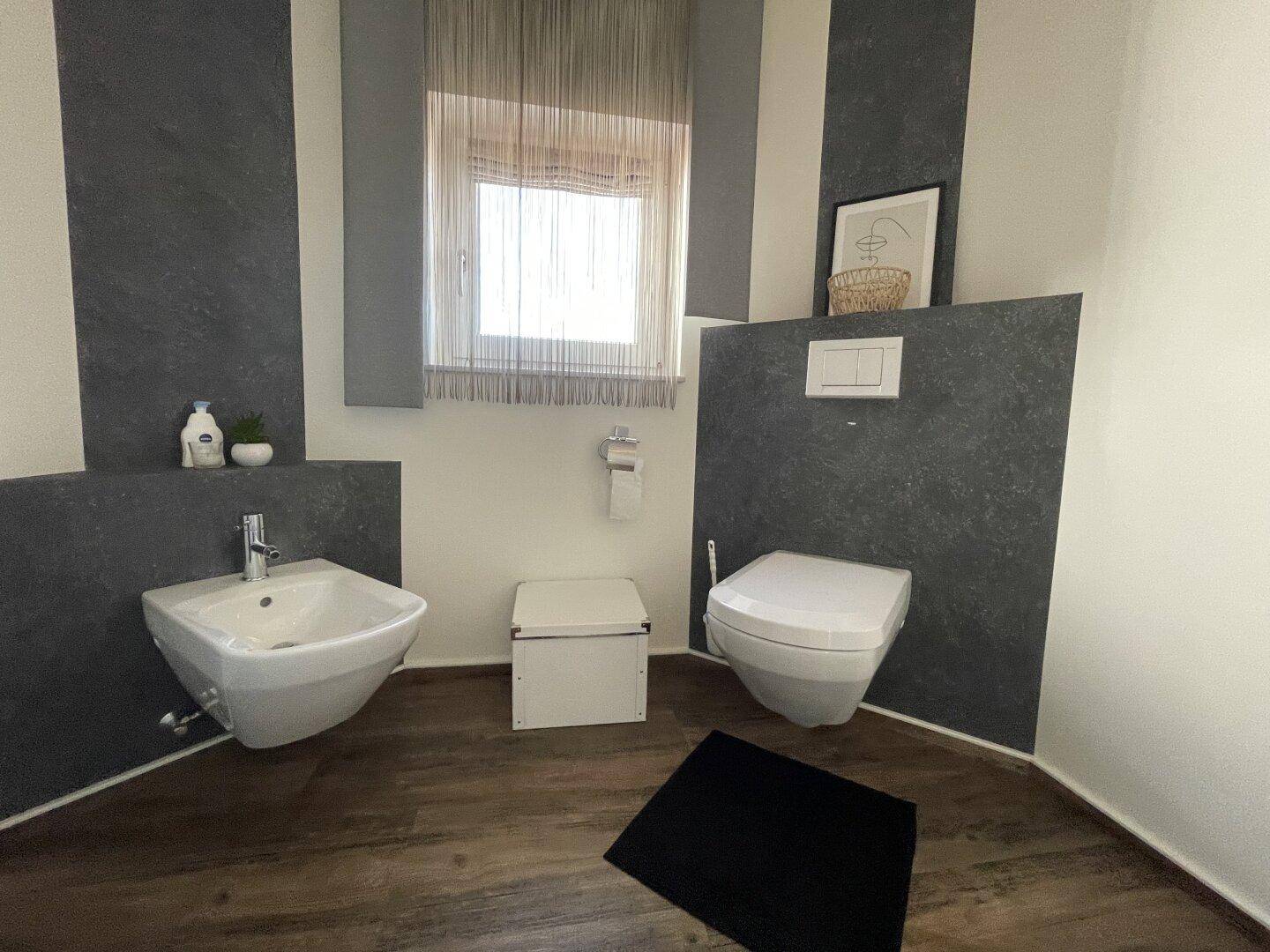 Helles Gäste-WC mit modernem Design, Bidet und wandhängender Toilette, ergänzt durch ein Fenster.