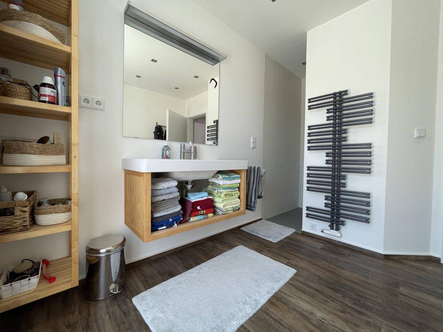 Modernes Badezimmer mit Waschtisch, offenem Holzregal und einem praktischen Handtuchheizkörper.