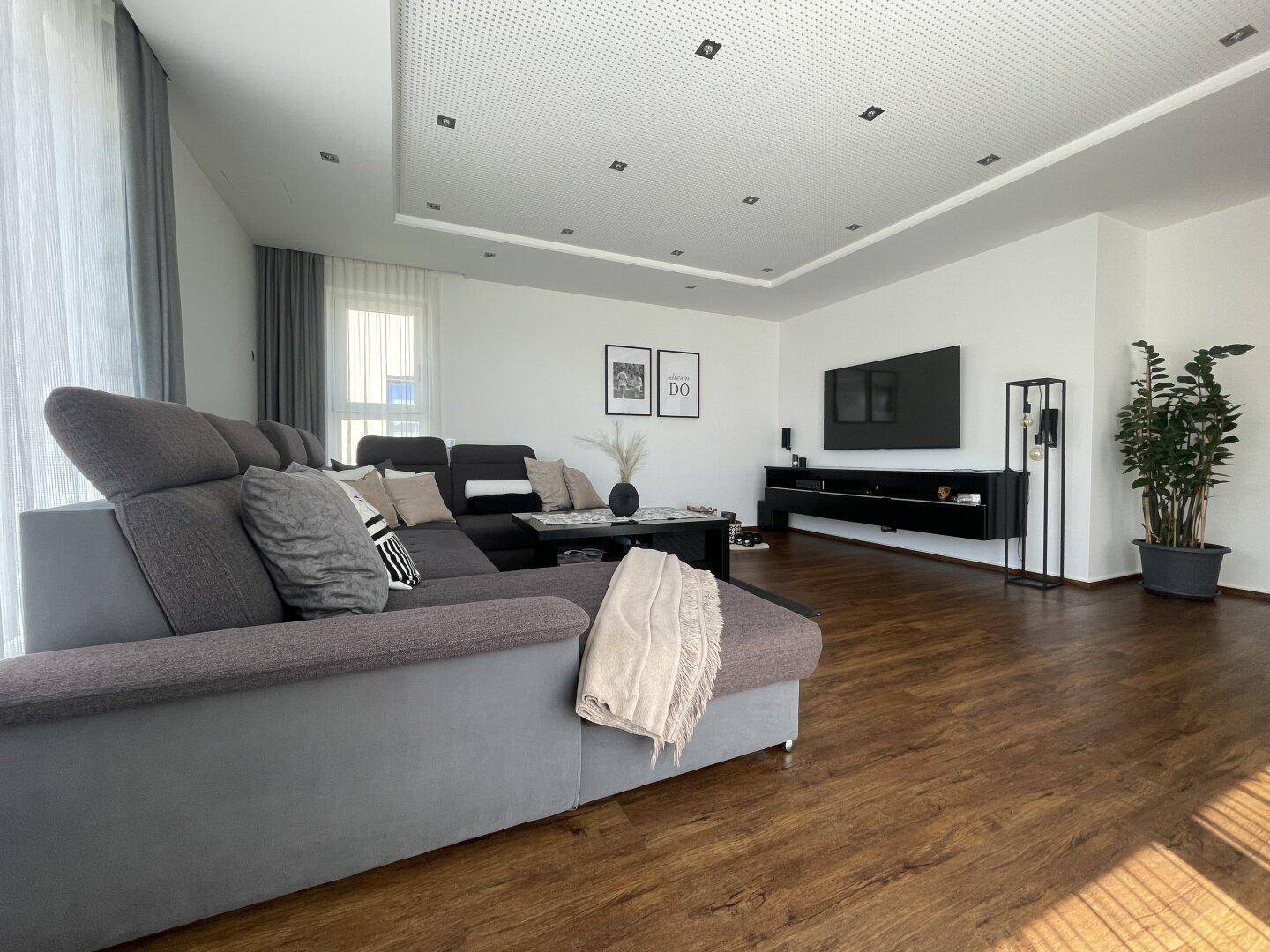 Modernes Wohnzimmer mit grauer Eckcouch, schwarzem Medienschrank und Holzoptikboden, der Wärme ausstrahlt.