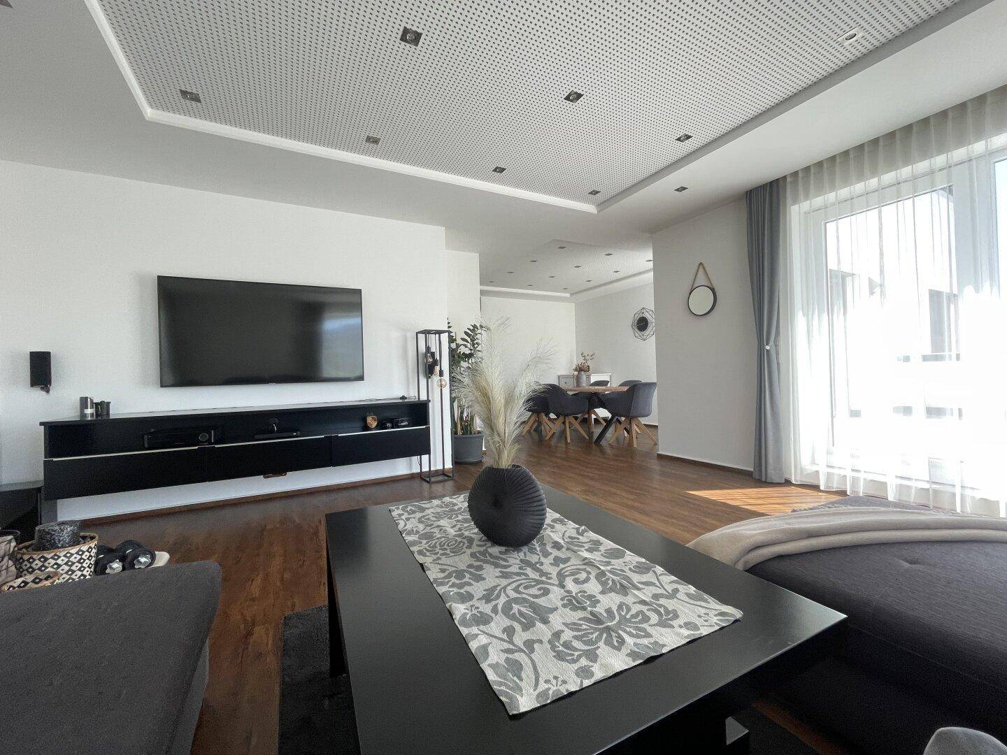 Offener Wohn- und Essbereich mit großem Fernseher, modernem Couchtisch und viel natürlichem Licht.