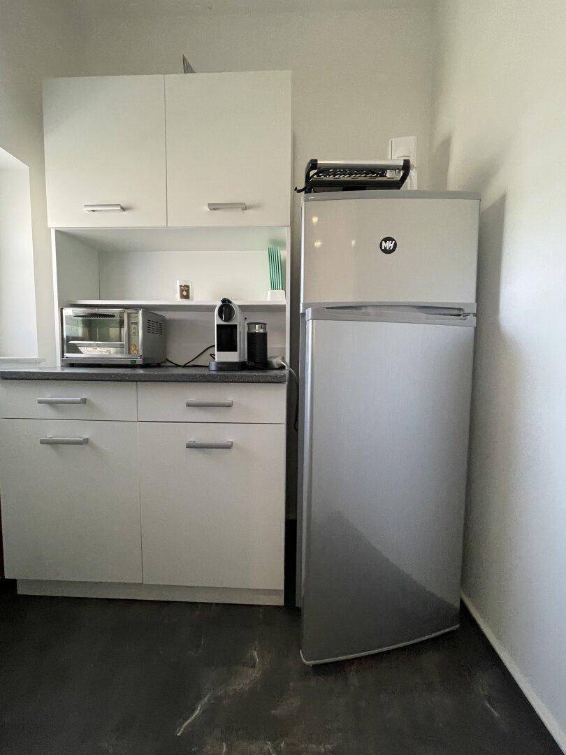 Kompakte Küchenzeile mit weißen Schränken, Kühlschrank und Mikrowelle, ideal für kleine Räume.