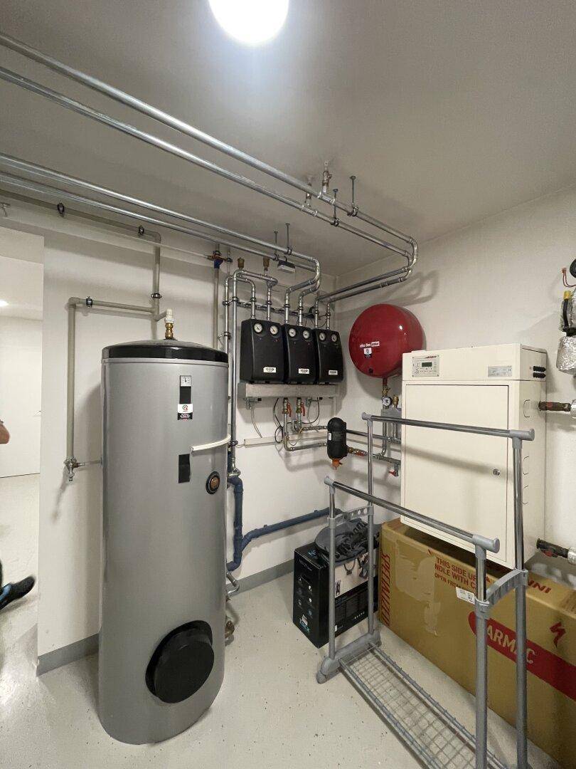 Technikraum mit moderner Heizungsanlage, Warmwasserspeicher und sichtbaren Rohrleitungen, gut organisiert.