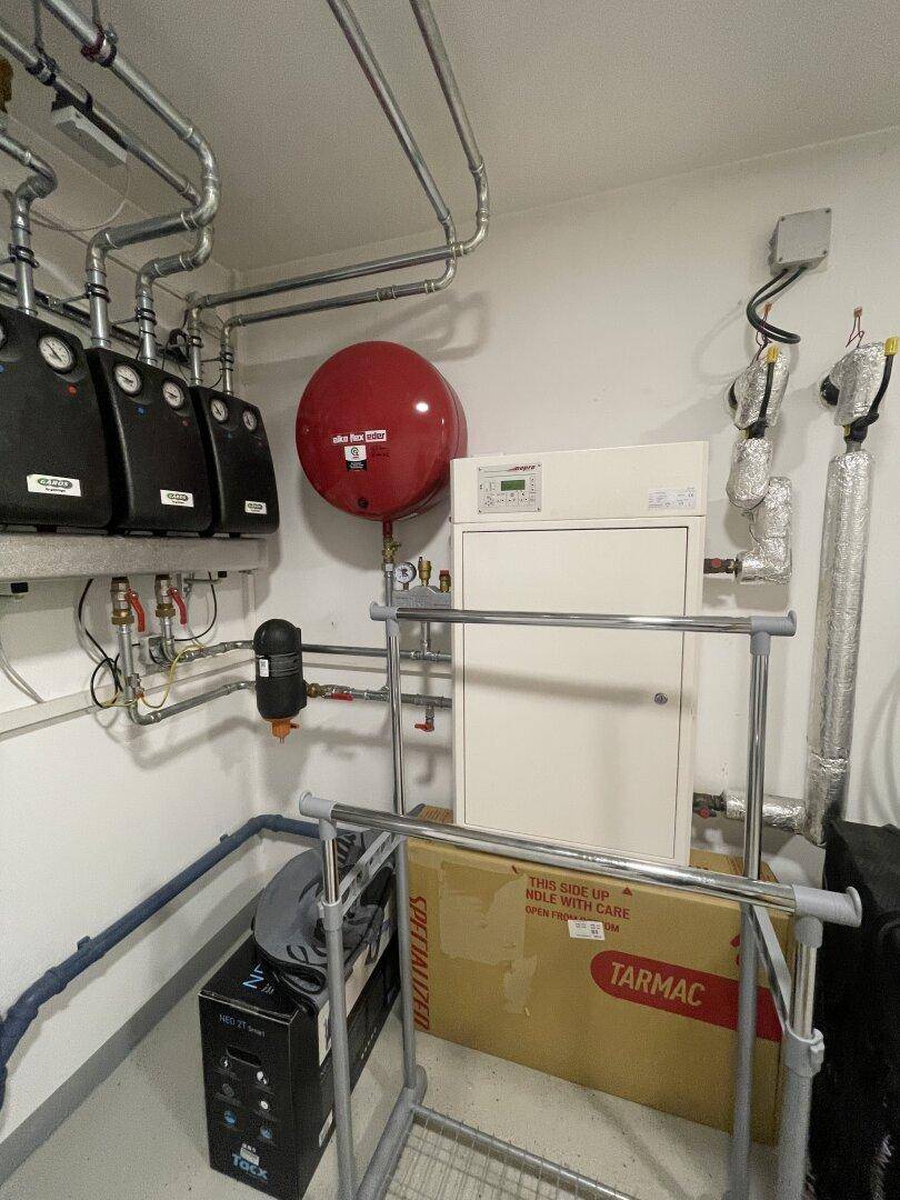 Detailansicht der Heizungsanlage und des Warmwasserspeichers im Technikraum, mit ordentlichen Installationen.
