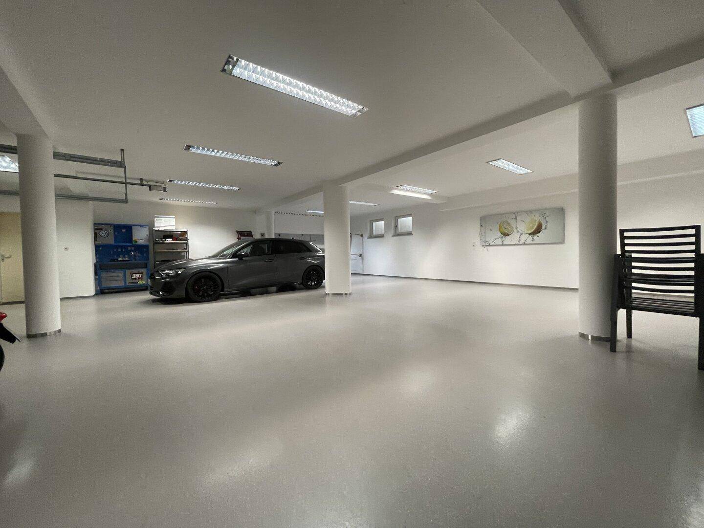 Weitläufige Tiefgarage mit einem geparkten Auto, Lagerbereichen und mehreren Fenstern für Tageslicht.