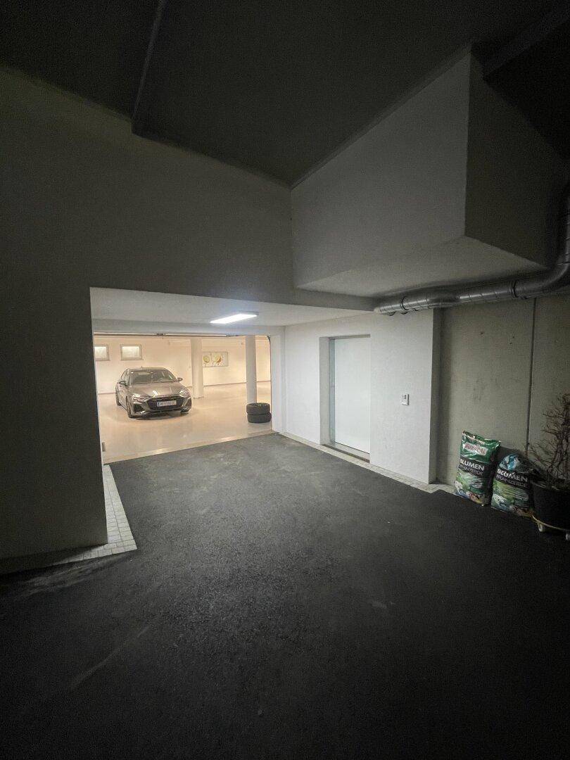 Dunkler Eingangsbereich einer Tiefgarage, der zu einem helleren, geräumigen Parkbereich mit einem Auto führt.