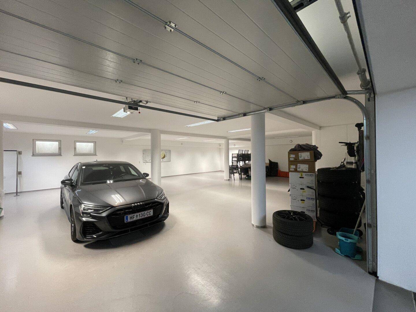 Detailansicht eines geparkten Autos in der geräumigen Tiefgarage mit offenem Garagentor und Lagerflächen.