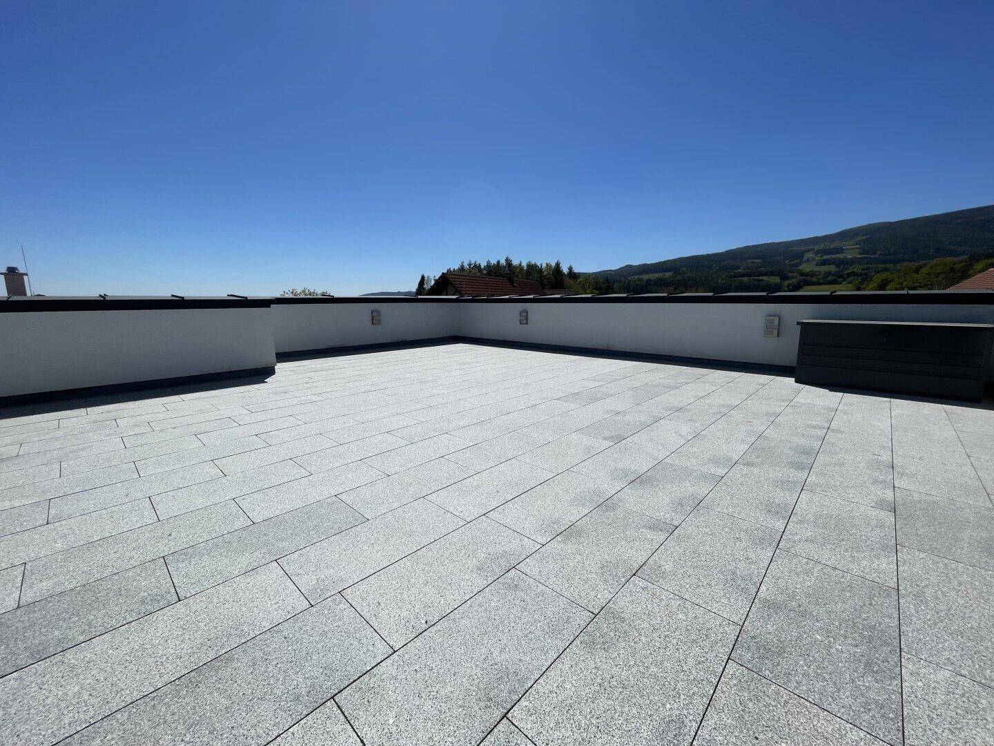 Weitläufige, geflieste Dachterrasse mit klarem Himmel und Panoramablick auf die umliegende Landschaft.