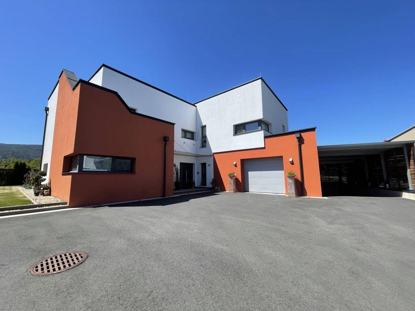 Moderne Hausfassade mit integrierter Garage und großzügiger Auffahrt, umgeben von Grünflächen.