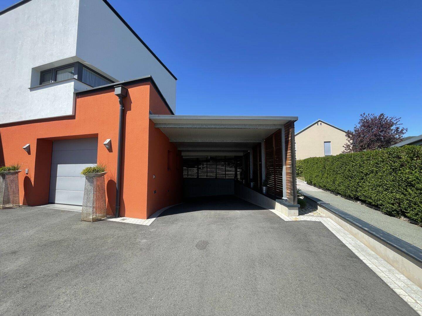 Modernes Haus mit orangefarbener Fassade, integrierter Garage und einem überdachten Carport.