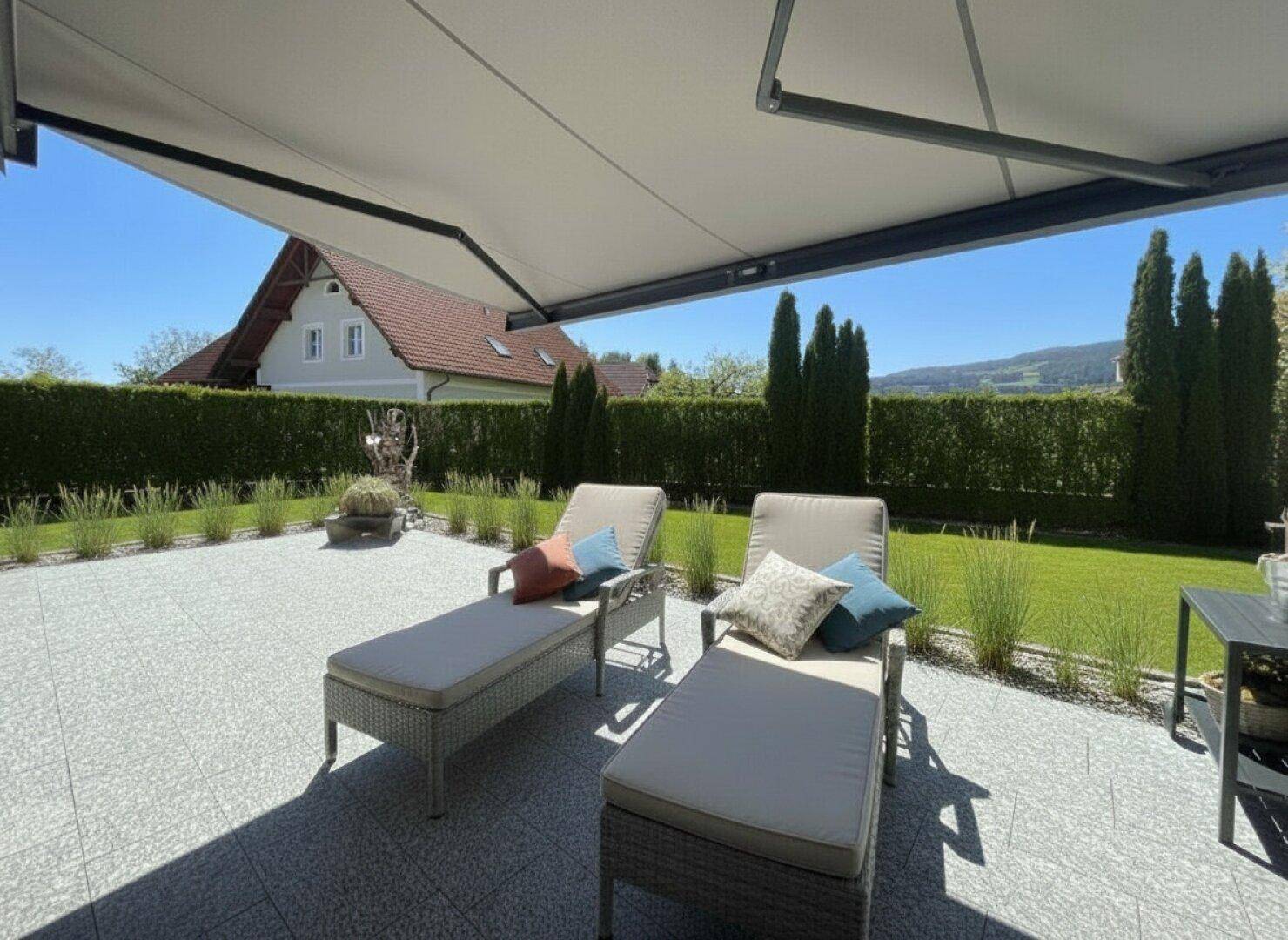 Gemütliche Terrasse mit Sonnenliegen und ausfahrbarer Markise, umgeben von einem gepflegten Garten.