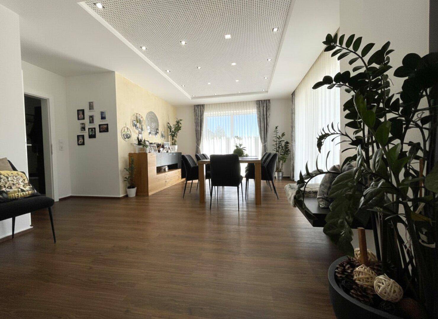Eleganter Essbereich mit großem Esstisch, dunklen Stühlen und Holzboden, offen zum Wohnbereich.