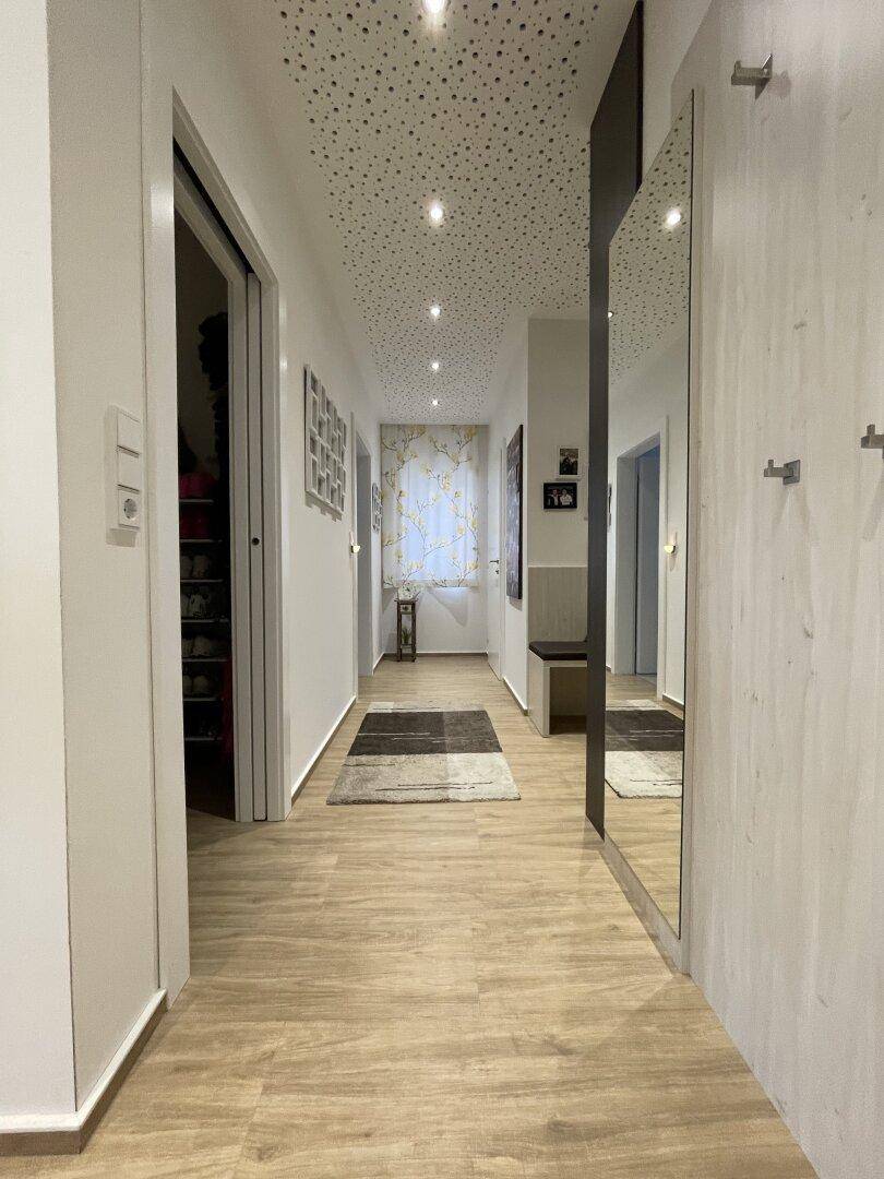 Langer Flur mit Holzboden, Einbauschränken und indirekter Beleuchtung an der Decke.