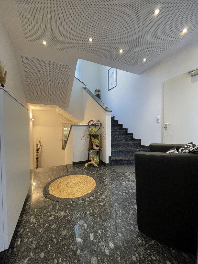Geräumiger Flur mit dunklem Granitboden, einer Treppe und einem einladenden schwarzen Sessel.