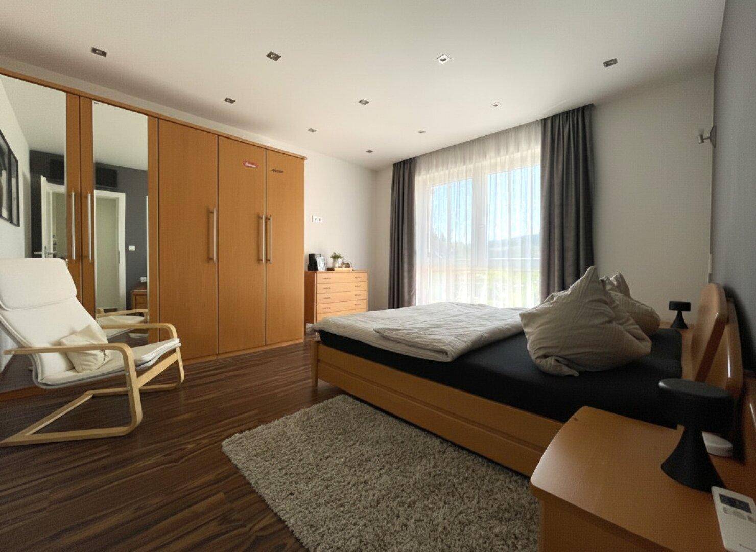 Geräumiges Schlafzimmer mit Holzbett, großem Kleiderschrank mit Spiegeltüren und Holzoptikboden.