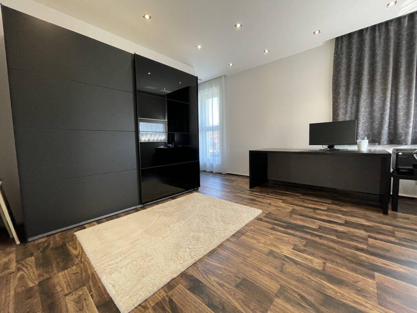 Modernes Arbeitszimmer mit großem schwarzem Kleiderschrank, schwarzem Schreibtisch und Holzoptikboden.